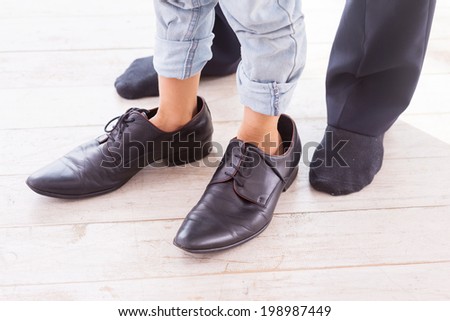 A little bit oversized. Close-up of child wearing large shoes while his father standing in socks near him