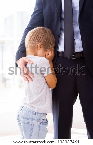 I will be missing you! Little boy crying and covering face with hands while his father in formalwear consoling him