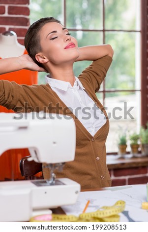 Satisfied with work done. Satisfied young fashion designer holding hands behind head and keeping eyes closed while sitting at her working place