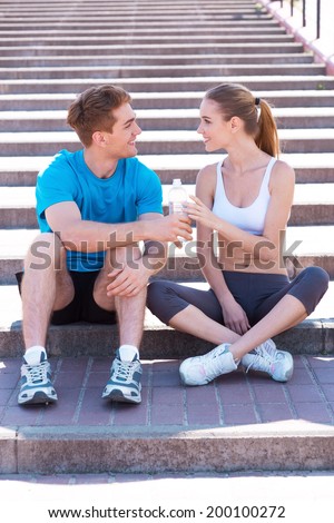 Sport connecting people. Side view of beautiful young couple in sports clothing sitting on stairs face to face and smiling