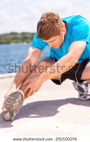 Stretching before running. Handsome young man doing stretching exercises and smiling while standing outdoors