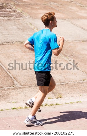 Enjoying a morning run.  Side view of young man running along the road