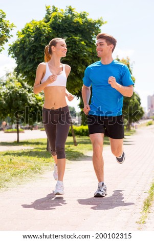 Jogging together.  Full length of young woman and man in sports clothing running along the road