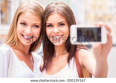 Women making selfie Two attractive young women making selfie and smiling while standing outdoors Women making selfie Two attractive young women making selfie and smiling while standing outdoors