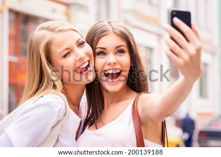 Friends making selfie Two beautiful young women making selfie and grimacing Friends making selfie Two beautiful young women making selfie and grimacing