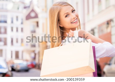 Nice day for shopping. Rear view of beautiful young cheerful woman holding shopping bags and looking over shoulder while standing outdoors