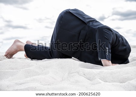 Hiding from his problems. Barefoot man in formalwear hiding his head in sand