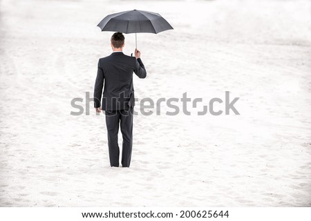 Safe business. Rear view of man in formalwear holding umbrella overhead while standing in desert