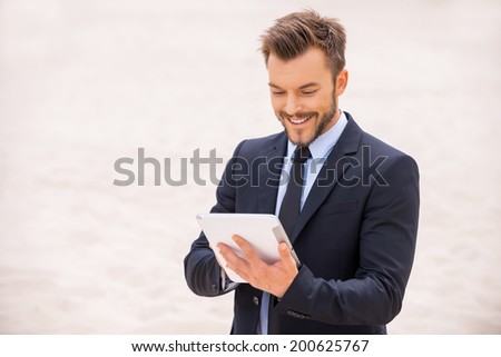 Surfing the net in desert. Cheerful young man in formalwear working on digital tablet while standing in desert