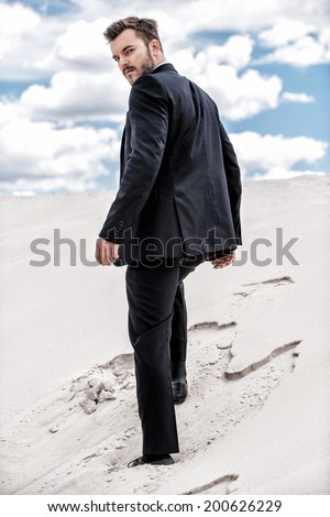 He is on his way to success. Rear view of young man in formalwear rising up by desert dune