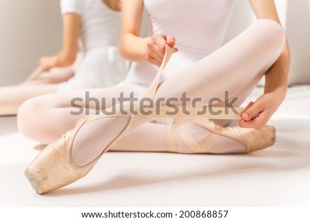 Tying ballet slippers. Close-up of ballerina in white tutu tying her slippers while sitting near the mirror