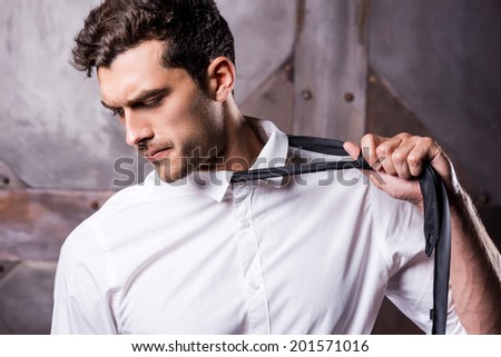 Taking his necktie away. Tired young man in formalwear taking off his necktie and looking away