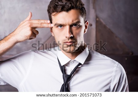 Corporate suicide. Tired young man in shirt and tie gesturing handgun near his head and looking at camera