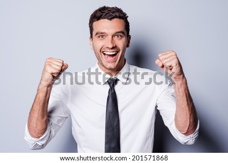 Successful businessman. Happy young man in shirt and tie gesturing and smiling while standing against grey background