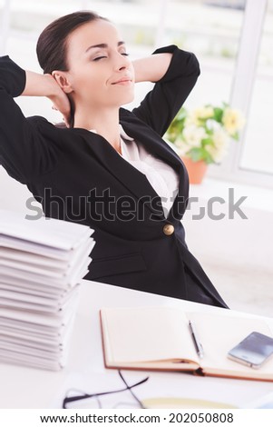 Chill time. Side view of cheerful young business woman holding head in hands and keeping eyes closed while sitting at her working place