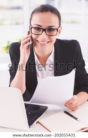 Confident businesswoman at work. Happy young woman in formalwear talking on the mobile phone while sitting at her working place