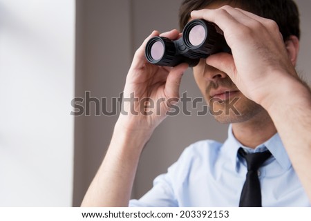 Looking for new opportunities. Confident young man in shirt and tie looking through binoculars