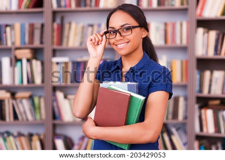 Feeling confident about exams. Cheerful African female student holding books and smiling while standing in library
