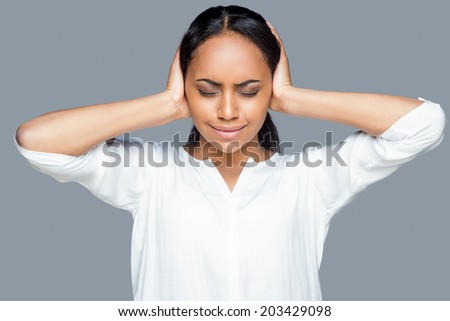 Feeling tired and stressed. Frustrated young African woman covering ears with hands and keeping eyes closed while standing against grey background