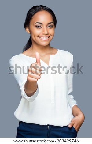 Beauty with thumb up. Waist up of attractive young African woman showing her thumb up and smiling while standing against grey background