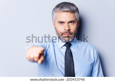 I made my choice. Confident mature man in shirt and tie looking at camera and pointing you while standing against grey background