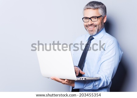 Supporting your business. Confident mature man in formalwear working on laptop while standing isolated on white background