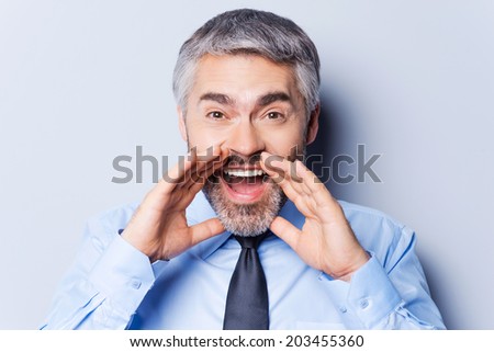 Sharing good news with you. Happy mature man in shirt and tie shouting while standing against grey background