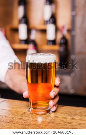 Quench your thirst! Close-up of man stretching out glass with beer while standing at the bar counter