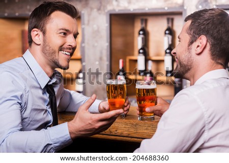 Friday night fun Two cheerful young men in shirt and tie talking to each other and gesturing while drinking beer at the bar counter Friday night fun Two cheerful young men in shirt and tie talking to each other and gesturing while drinking beer at the bar counter