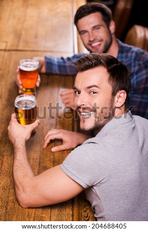 Friends in bar. Top view of two happy young men drinking beer at the bar counter and smiling