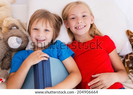 Little bookworms. Top view of two cute children holding book while lying in bed together