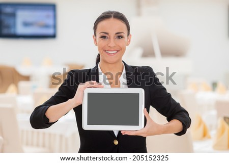 Copy space on her tablet. Beautiful young woman in formalwear showing her digital tablet and smiling while standing in restaurant
