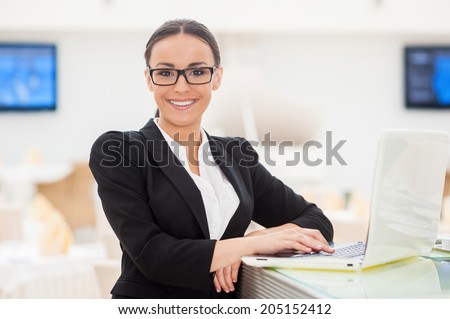 Successful business lady. Beautiful young woman in formalwear working on laptop and smiling while leaning at bar counter