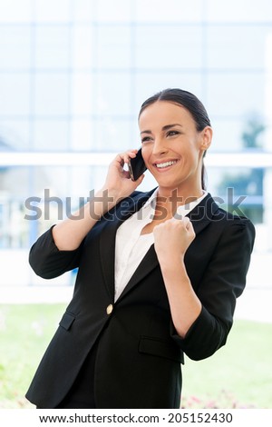 Business winner. Beautiful young woman in formalwear talking on the mobile phone and gesturing while standing outdoors