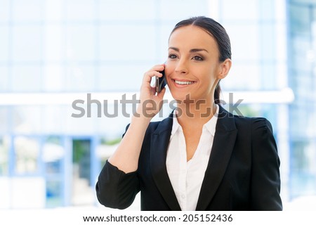 Staying connected. Beautiful young woman in formalwear talking on the mobile phone and smiling while standing outdoors
