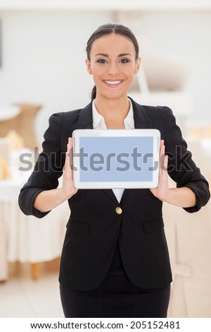 Your message on her tablet. Attractive young woman in formalwear showing her digital tablet and smiling while standing in restaurant