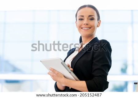 Taking advantages of digital age. Beautiful young woman in formalwear holding digital tablet and smiling while standing outdoors
