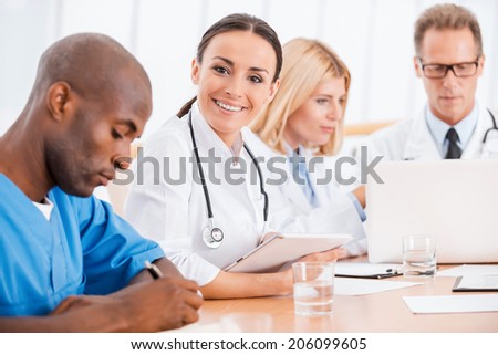 Doctor at the meeting. Beautiful young female doctor smiling while sitting together with her colleagues at the meeting