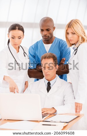 They all need an expert advice. Group of confident doctors discussing something while looking at the laptop together