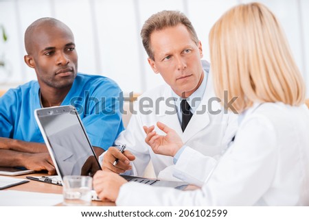 Doctors at the meeting. Three confident doctors discussing something while woman using computer and gesturing