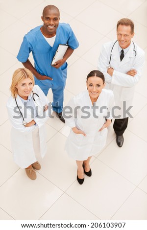 Always ready to help. Top view of four confident doctors standing close to each other and smiling