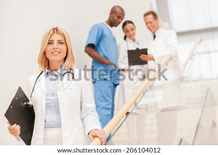 Confident female doctor. Confident female doctor moving downstairs and smiling while her colleagues talking in the background