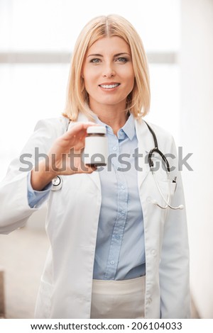 Healing medicines. Confident female doctor in white uniform holding container with medicines and smiling