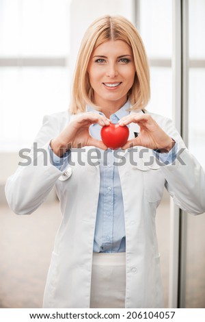 Your heart in good hands. Confident female doctor in white uniform holding heart prop and smiling