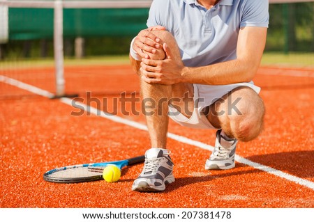 Sports injury. Close-up of tennis player touching his knee while sitting on the tennis court
