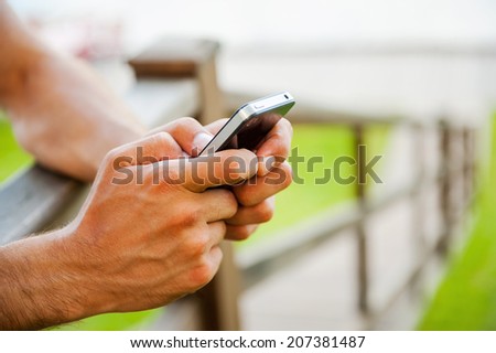 Message to a friend. Close-up of man typing message on mobile phone while standing outdoors