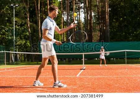 Preparing to his best serve. Full length of man and woman playing tennis on tennis court