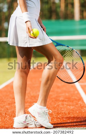 Elegant and sporty. Close-up of beautiful woman in sports clothing holding tennis racket and ball while standing on court