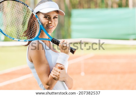 Are you ready to play?  Side view of beautiful young woman in sports clothing holding tennis racket and smiling