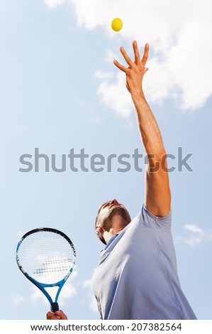 Serving a ball. Low angle view of tennis player serving a ball while standing against blue sky
